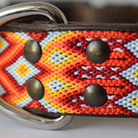 Close-up of a woven leather collar with a colorful geometric pattern in red, orange, yellow, white, and blue, featuring dark metal rivets and a silver-tone D-ring.