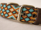 A close-up of a woven leather collar with a geometric diamond pattern in brown, orange, turquoise, and cream, featuring a polished silver buckle.