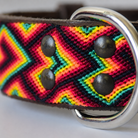 Close-up of a woven leather belt strap with a bold chevron pattern in red, yellow, green, and black, featuring dark metal rivets and a silver metal D-ring.